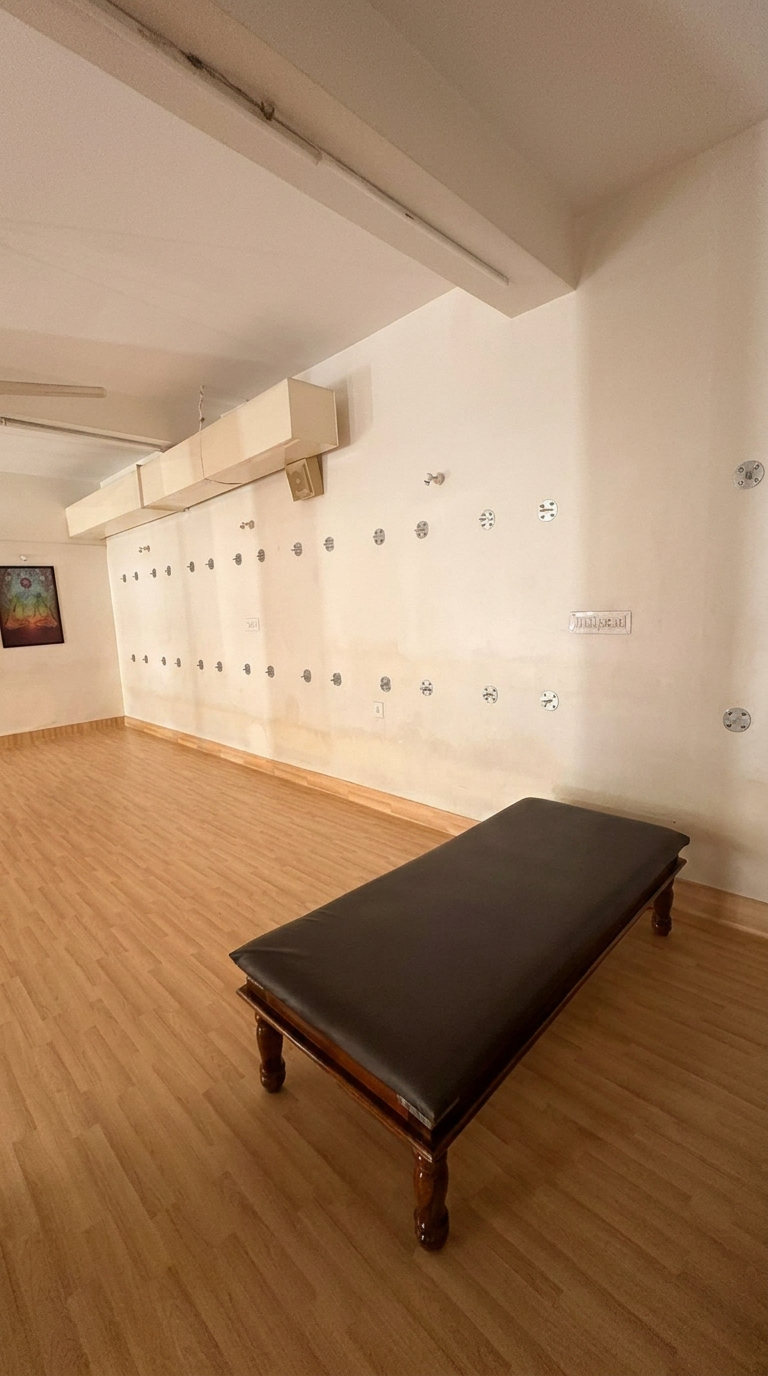 Spacious therapy hall with a leather-topped wooden treatment bench, warm wooden flooring and a clean white wall
