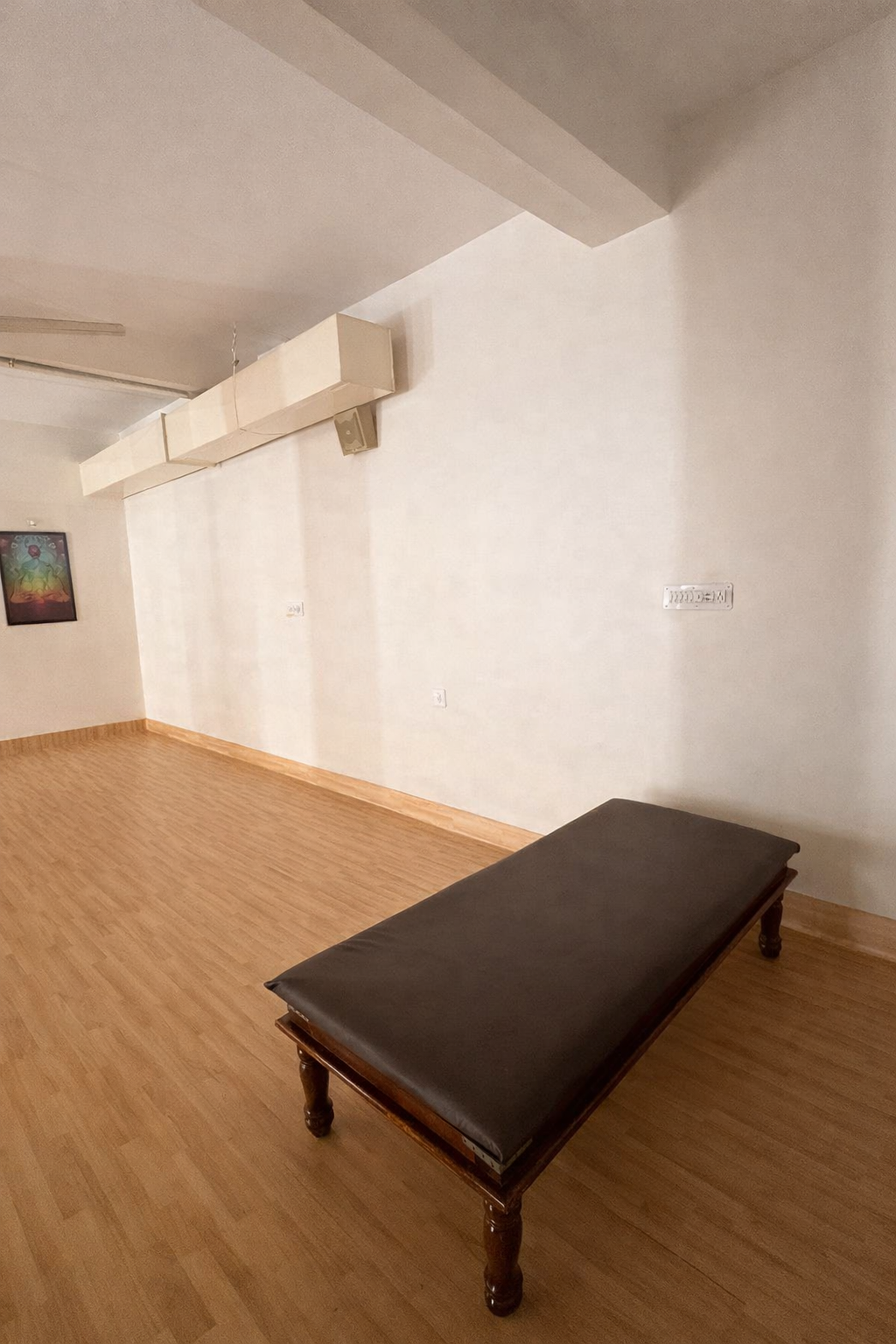 Therapy hall with a leather-topped wooden treatment bench, warm wooden flooring and clean white walls