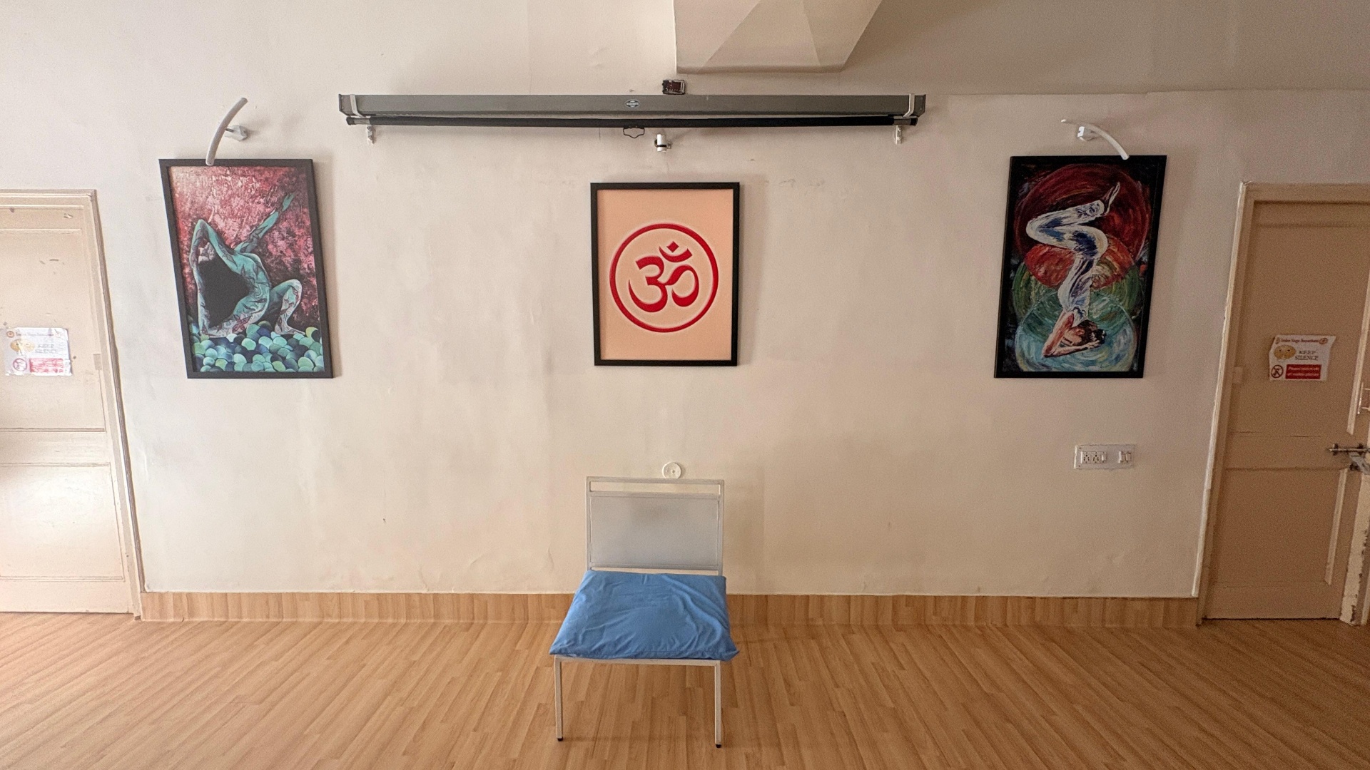 Three framed artworks — a figure in red, the Om symbol centred, a green & red figure — above a single chair