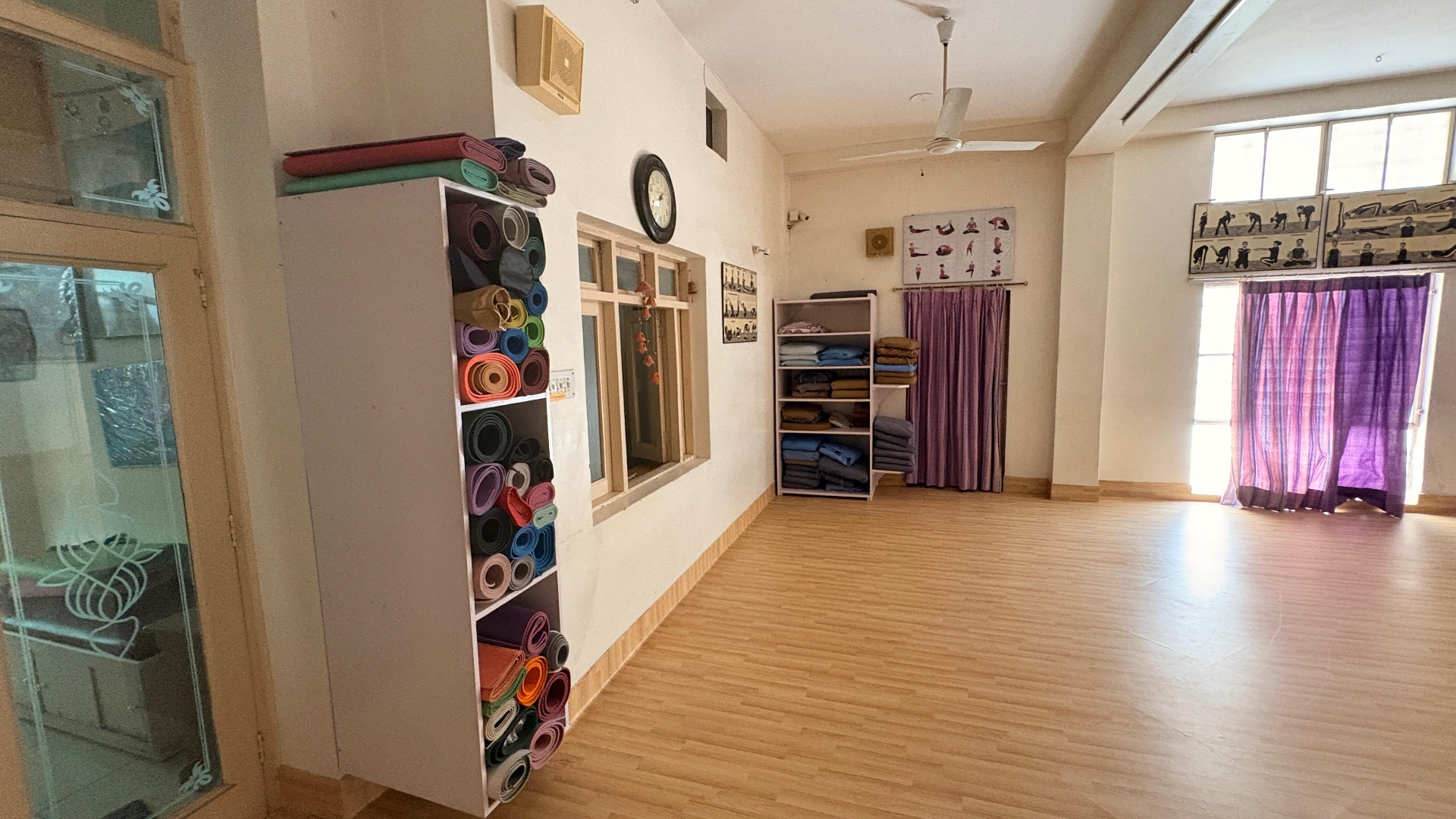 Tall mat-storage shelf filled with rolled yoga mats beside folded blankets and purple curtains