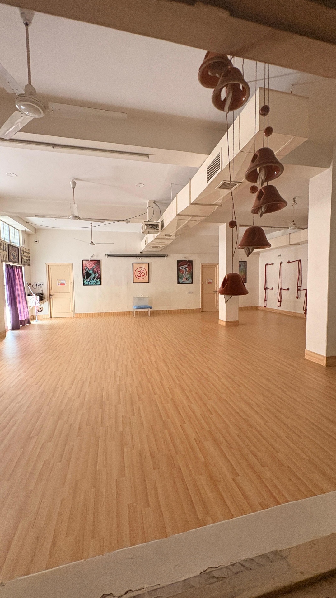 Main yoga hall with wooden floor, ropes and hanging clay bells