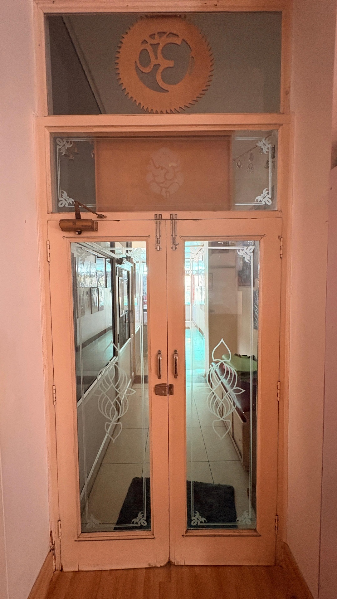 Etched-glass double entrance doors with the copper Om medallion and Ganesha motif above